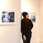 Leah Oates leans among her works, displayed on the white walls of a gallery.